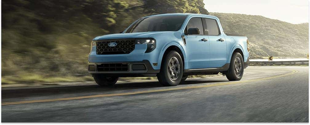 Light blue 2026 Ford Maverick pickup truck driving along a curved paved road.