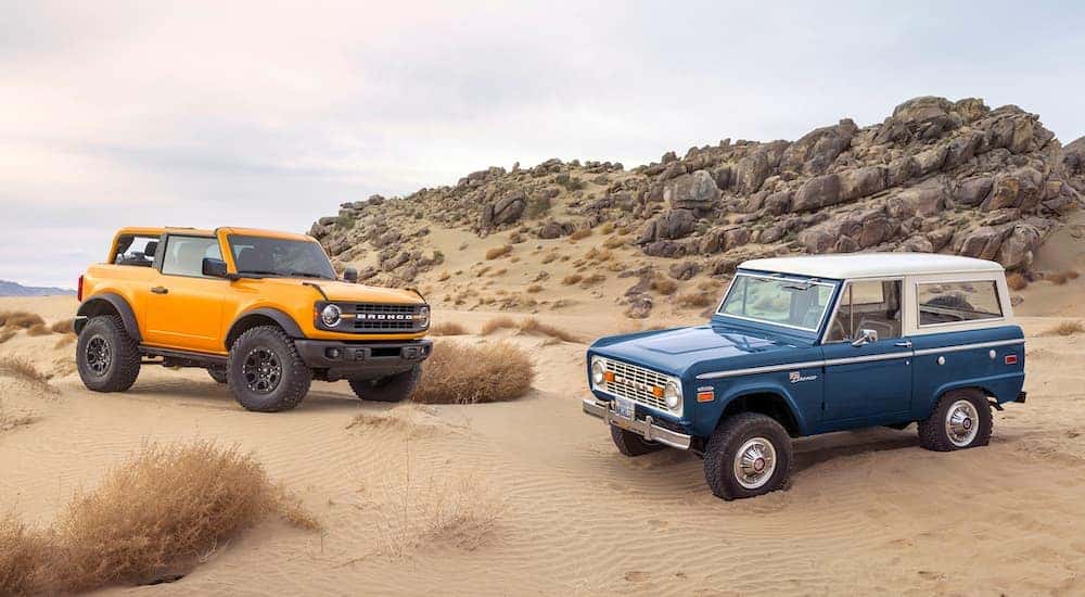 A yellow 2021 Ford Bronco and a blue 1966 Ford Bronco parked together on rocky sand dunes