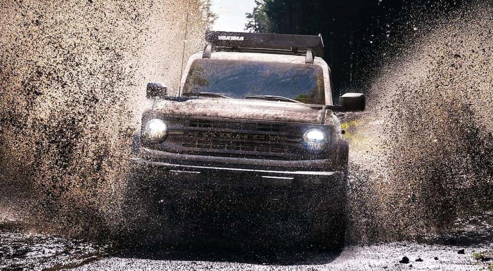 Seen from the front, a Silver Ford Bronco splashes through the mud