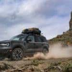 A black Ford Bronco Sport Outer Banks spins its wheels in the dirt in front of jagged mountains
