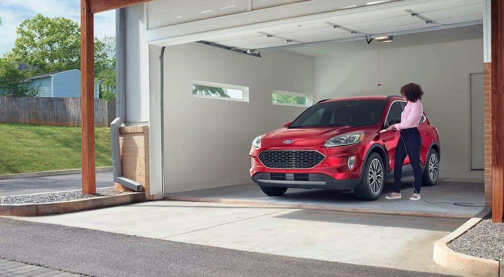 In a modern garage, a woman plugs in her red 2020 Ford Escape Plug-In Hybrid.