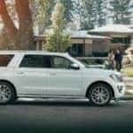 A couple walks to a white Ford Expedition parked in front of their modern suburban home