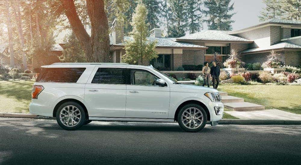 A couple walks to a white Ford Expedition parked in front of their modern suburban home