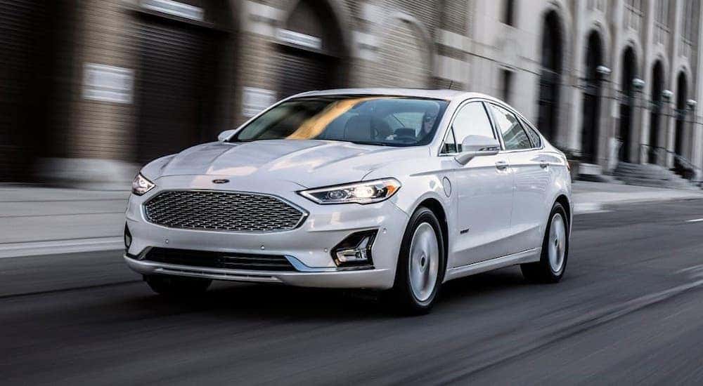 A white Ford Fusion hybrid drives down a city street near Canon City, CO