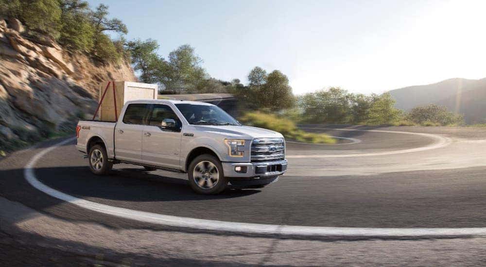 A white 2016 Ford F-150 with a large box in the bed driving around a tight curve.