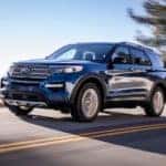 A blue 2021 Ford Explorer is driving on a highway in front of an evergreen tree after leaving a Ford Explorer dealer.