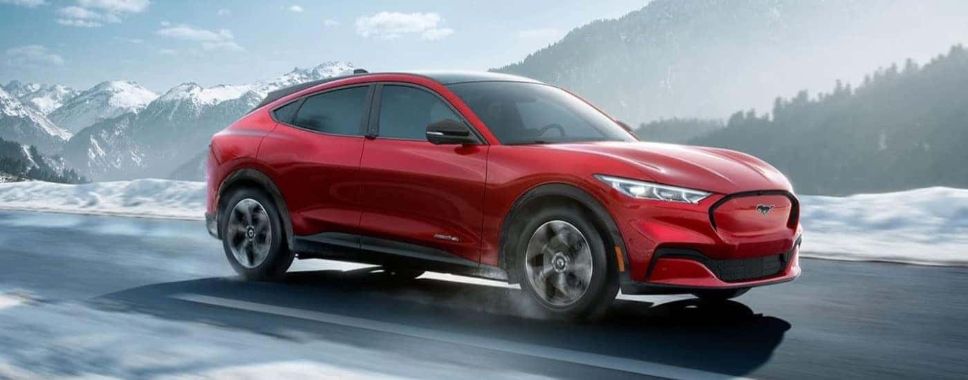 A red 2022 Ford Mustang Mach-E is shown driving past snowy mountains.