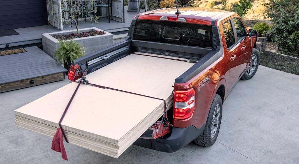 Sheets of plywood stacked in the bed of a red Ford Maverick Flexbed parked outside a house