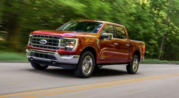 A red 2021 Ford F-150 is driving on a tree-lined highway.