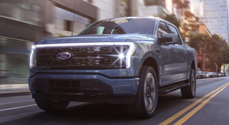 A blue 2022 Ford F-150 Lightning is shown driving through a city after leaving a Ford Lightning dealer.