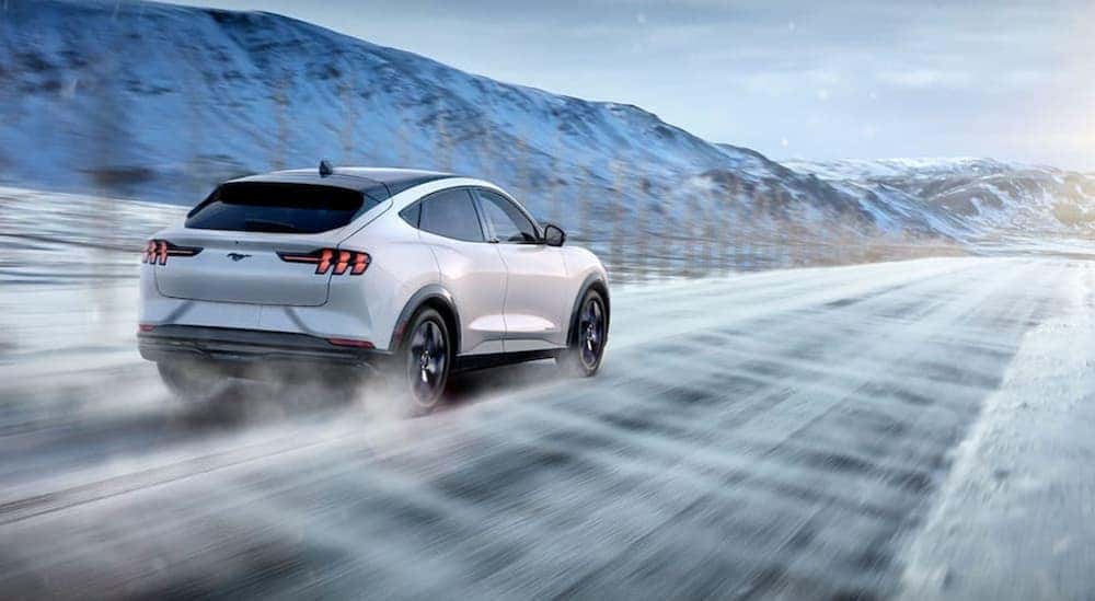 A white 2021 Ford Mustang Mach-E driving on a snowy road.