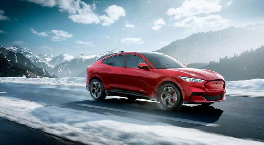A red Ford Mustang Mach-e Mustang drives on snow-covered roads with white mountains in the background
