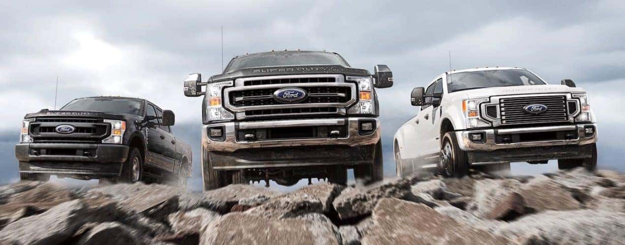 A black 2021 Ford Super Duty F-250, a black F-350, and a white F-450 are shown from the front from a low angle while climbing over rocks.