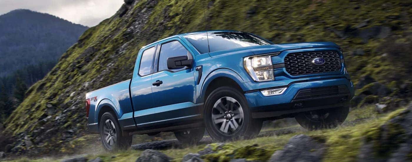 A blue 2021 Ford F-150 is shown from the side off-roading in the mountains.