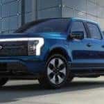 A blue 2022 Ford F-150 Lightning is shown parked outside of a modern glass building.