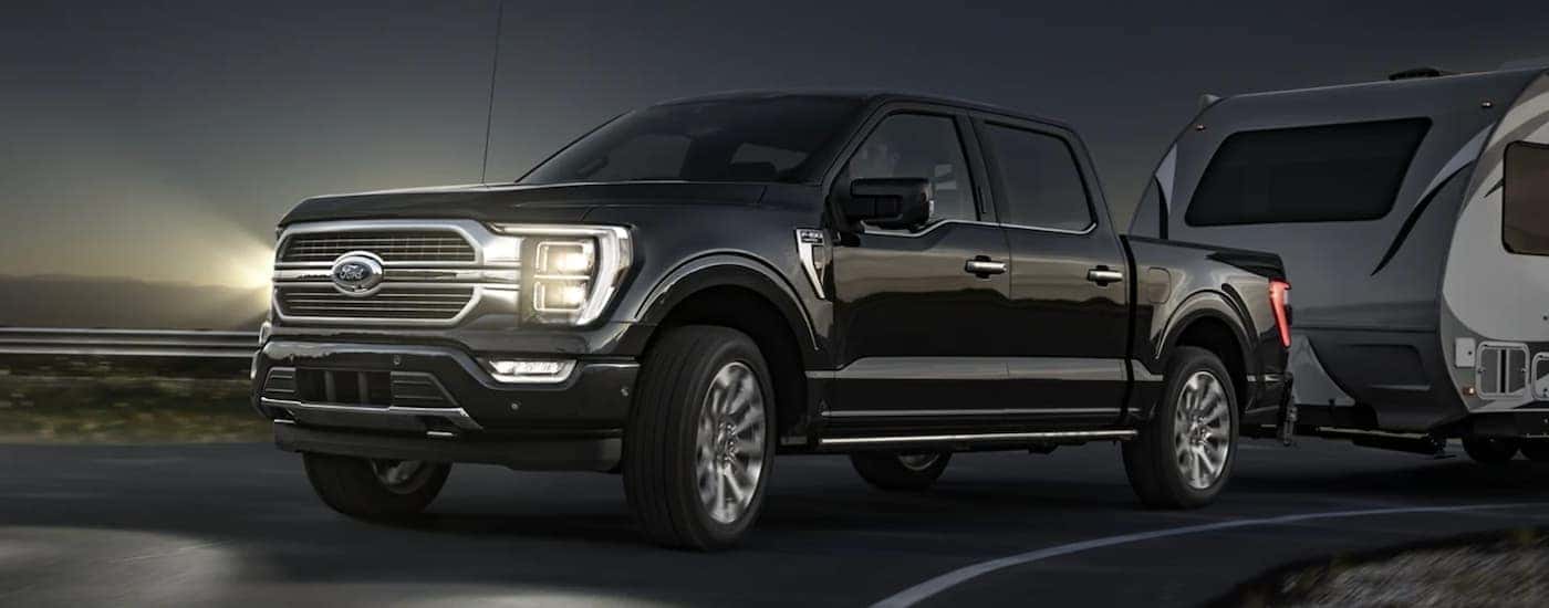 A black 2021 Ford F-150 is shown towing a closed trailer at night.