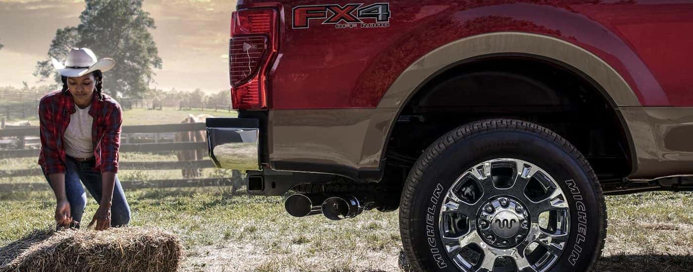 A person is shown loading hay bales into the bed of a red 2022 Ford F-350 Super Duty King Ranch FX4.