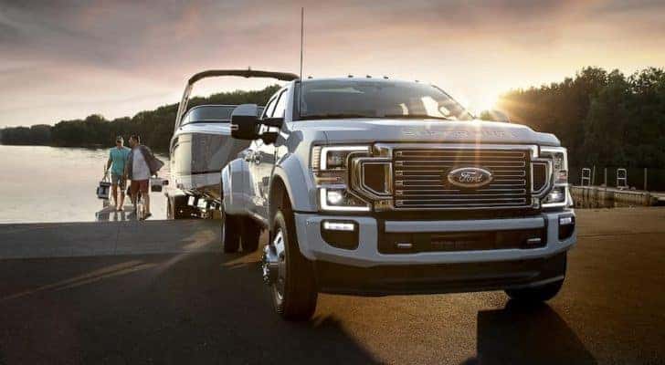 A white 2022 Ford F-450 Super Duty Limited is shown backing a boat into a lake.