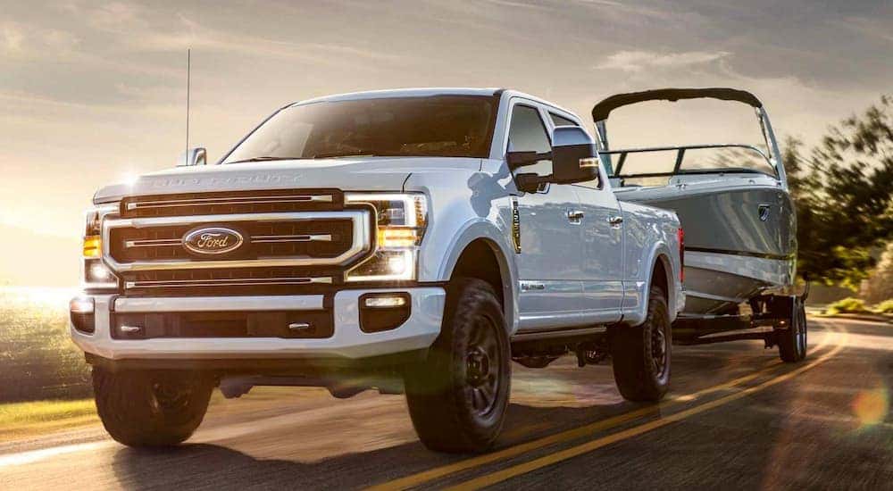 A white Ford Super Duty F-350 Lariat tows a motor boat along a sunny highway