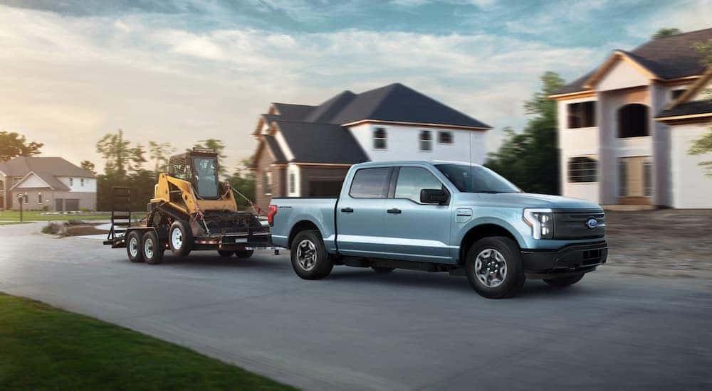 A blue Ford F-150 Lightning tows heavy equipment through a suburban neighborhood