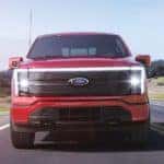 Front view of a red Ford F-150 Lightning driving down a rural highway