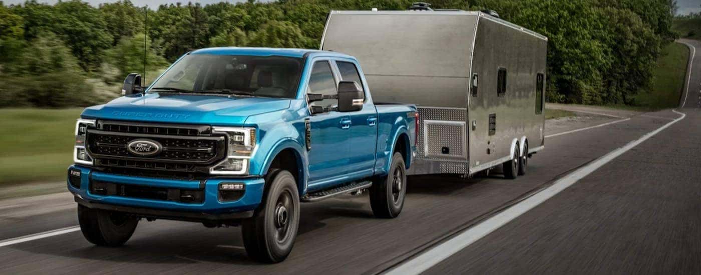 A blue 2020 Ford F-250 Super Duty is shown towing a camper on a highway.