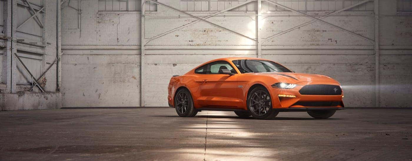 An orange 2020 Ford Mustang High Performance is shown from an angle parked in a warehouse.