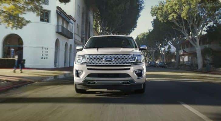 A white 2021 Ford Expedition is shown driving on a city street after leaving a Certified Pre-Owned Ford dealer.