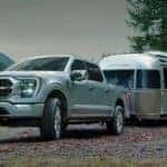 A silver 2022 Ford F-150 is shown towing a Airstream trailer near a lake.