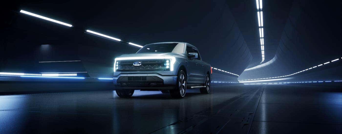 A light blue 2022 Ford F-150 Lightning is shown driving in a futuristic tunnel. 