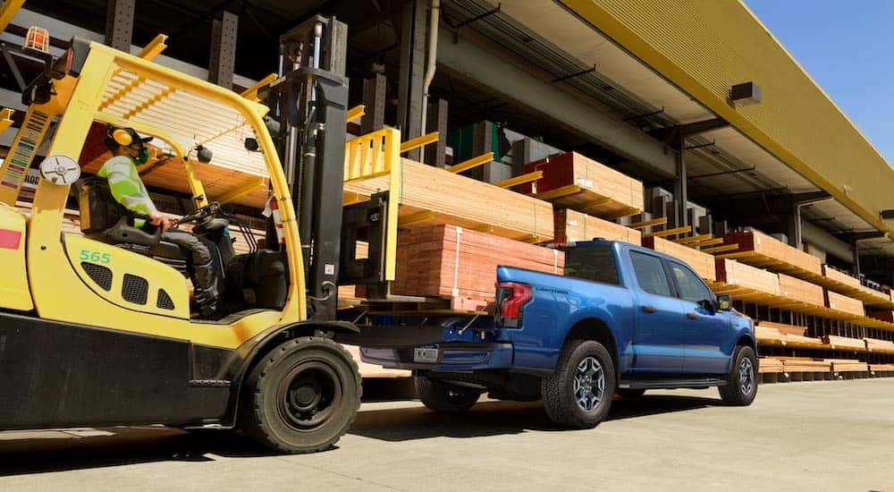 A blue 2022 Ford F-150 Lightning XLT is shown from behind being loaded with wood.