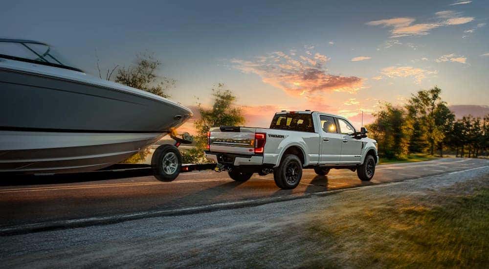 A white 2022 Ford F-250 Super Duty Tremor is shown towing a boat at dusk.