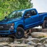 A blue 2022 Ford F-350 Super Duty Tremor is shown driving down a rock path after visiting a 2022 Ford Super Duty dealer.