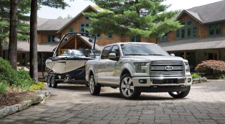 A white 2016 Ford F-150 Limited is shown towing a boat in a driveway after leaving a Ford F-150 dealer.