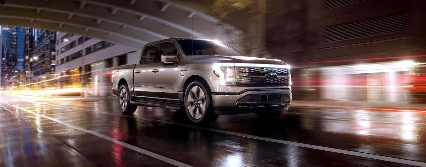 A silver 2022 Ford F-150 Lightning Platinum is shown driving through a city at night.