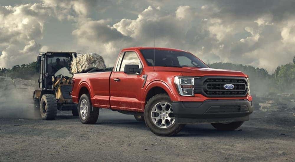 A red 2022 Ford F-150 is shown from the side parked towing a trailer after leaving a Ford F-150 dealer.