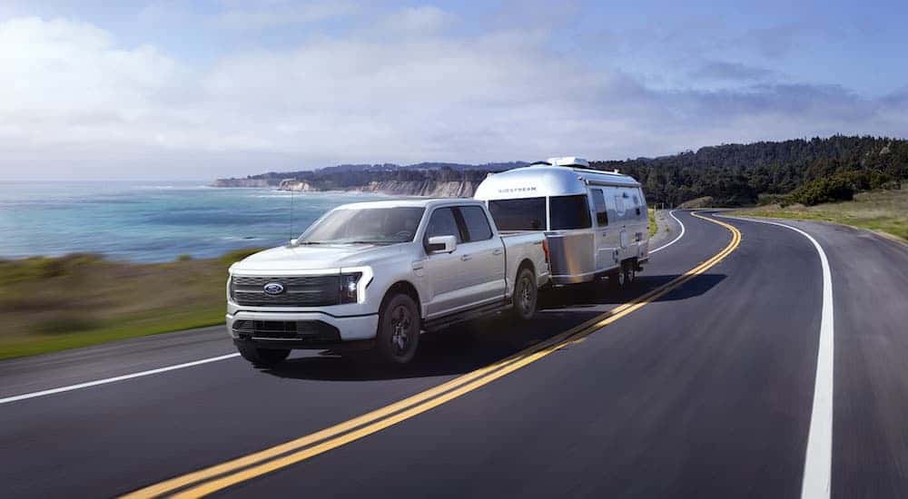 A white 2023 Ford F-150 Lightning is shown from the front at an angle while towing a mobile home.