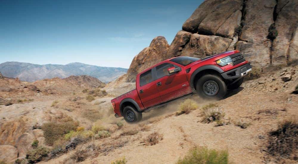 A red 2014 Ford F-150 Raptor is shown from the side while climbing a hill after leaving a dealer that has a Ford F-150 for sale near Rockvale, CO.