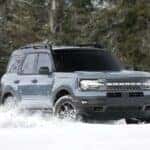 A grey 2023 Ford Bronco Sport Badlands is shown kicking up snow after looking at a Ford Bronco Sport for sale.