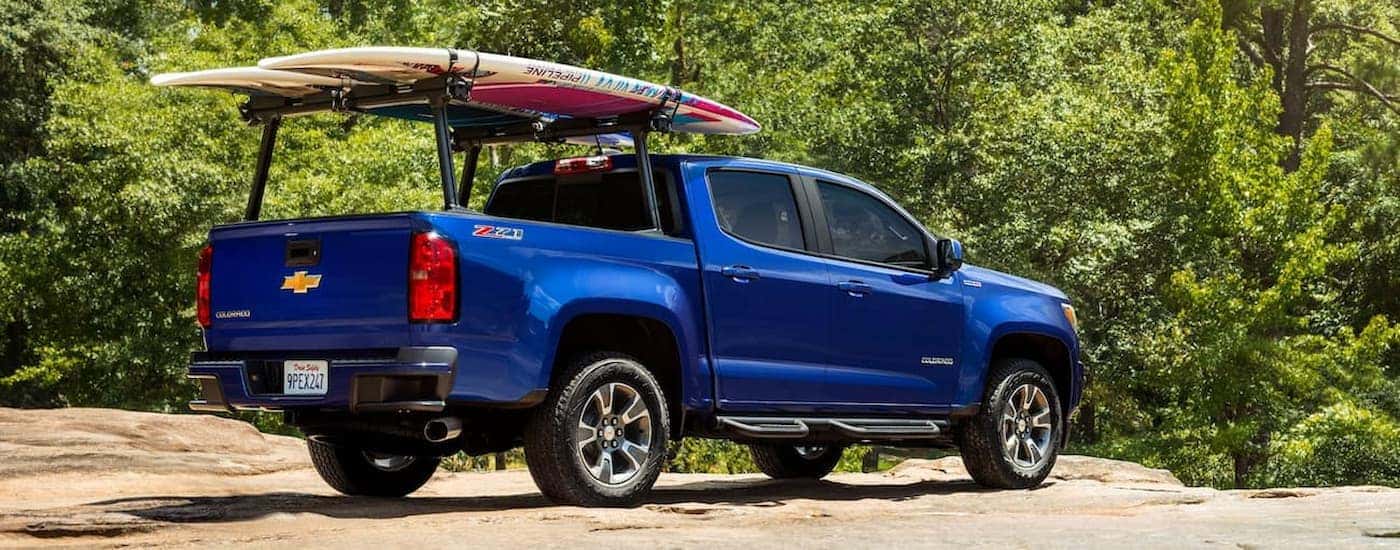 A blue 2019 Chevy Colorado is shown from a rear angle parked on with a surfboard attached to a rack.