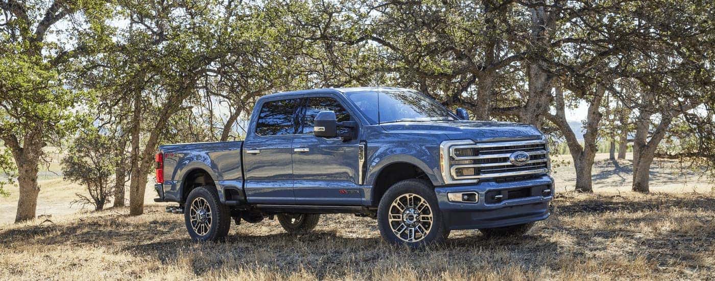 A blue 2023 Ford F-350 Super Duty is shown parked next to a row of trees.