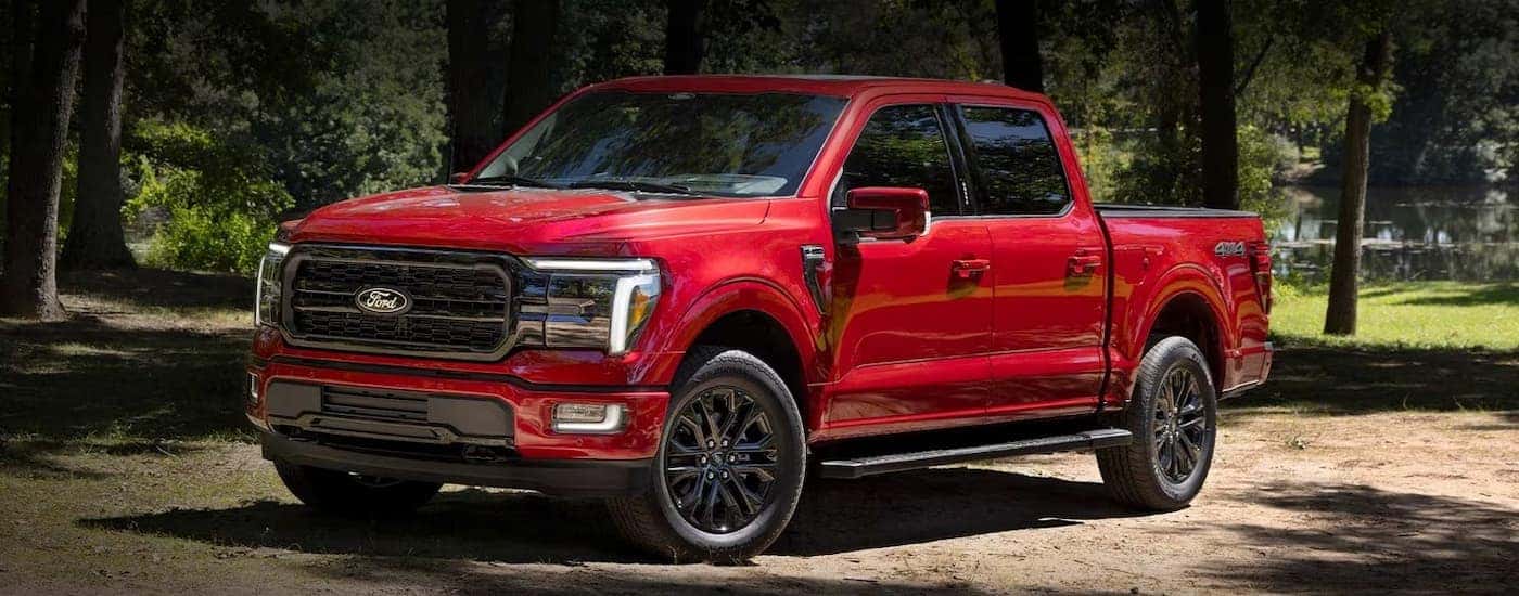 A red 2024 Ford F-150 is shown parked on a dirt road after leaving a truck dealer.