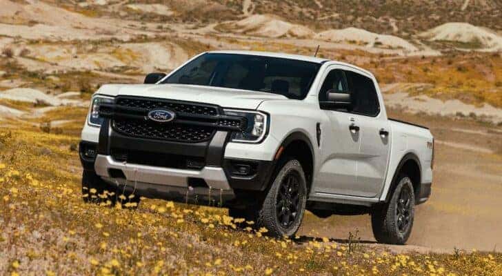 A white 2024 Ford Ranger is shown driving through a dusty field.