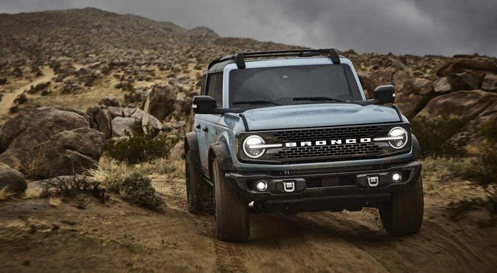 A blue 2021 Ford Bronco is shown driving on a trail.