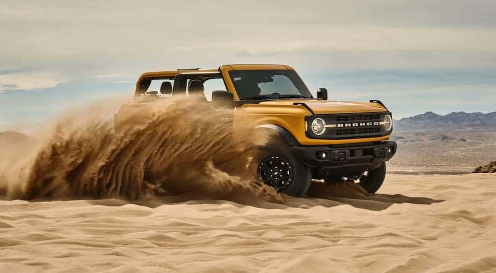 A yellow 2021 Ford Bronco is shown driving off-road through a desert.