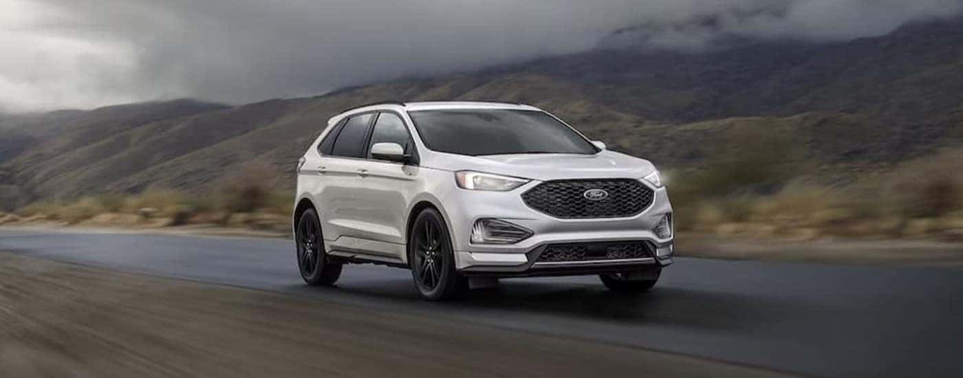A white 2023 Ford Edge is shown driving near mountains.