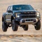 A dark green 2024 Ford F-150 Raptor is shown driving off-road after visiting a dealer with a Ford F-150 for sale near Pueblo West.