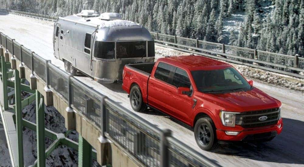 A red 2024 Ford F-150 Sport is shown towing a trailer across a snowy bridge after visiting a dealer with a Ford F-150 for sale near Pueblo West.