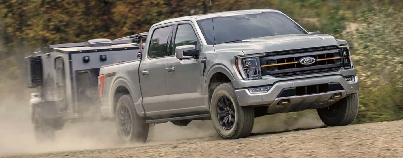 A tan 2024 Ford F-150 Tremor is shown towing a trailer on a dusty trail.
