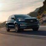A teal 2024 Ford Edge ST driving on a mountain highway.